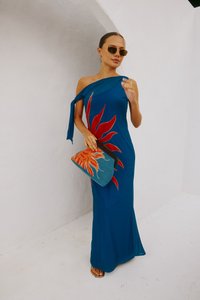 Abito blu a spalla unica con un motivo a fiamma rossa, realizzato in tessuto leggero. Completato da una pochette blu con perline e dettagli arancioni.
