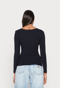 Haut en maille côtelée bleu marine à manches longues et encolure festonnée, cintré à la taille. Porté avec un jean taille haute bleu clair.