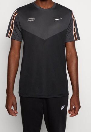 T-shirt de sport gris avec un motif en chevron, logos Nike en blanc, et des rayures multicolores sur les manches. Tissu doux, manches courtes.