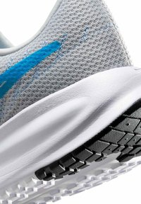 Jasnoszary but sportowy z oddychającą siateczkową cholewką, niebieskim akcentem i teksturowaną czarną gumową podeszwą z wzorzystym bieżnikiem.