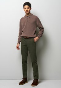Bruine gebreide polo met drie knopen, olijfgroene broek en bruin suède enkelboots met veters. Geweven stof en getailleerde pasvorm.