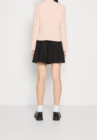 Světlé růžové přiléhavé sako s dlouhými rukávy, kombinované s černou rozšířenou sukní. Modelka má na sobě černé platformové boty a bílé kotníkové ponožky.