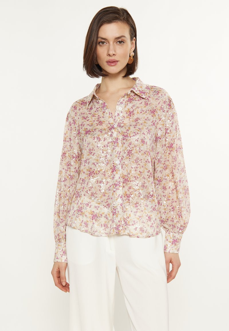 Bloemige zijden blouse met lange mouwen, knoopsluiting en paillettenaccenten. Lichtroze achtergrond met kleine paarse en gele bloemenpatronen.
