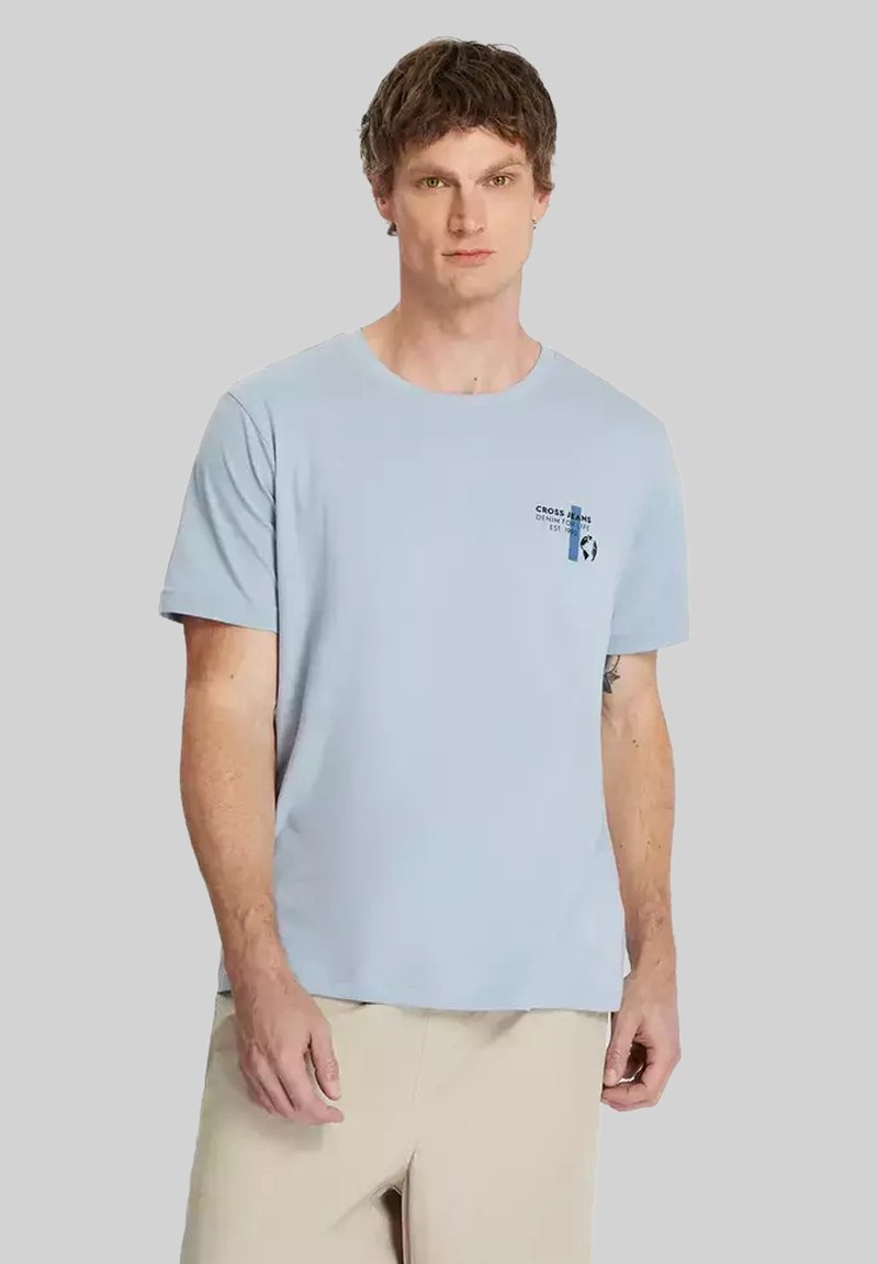 Jasnoniebieska koszulka z cienkiego materiału, z okrągłym dekoltem i krótkim rękawem. Małe logo na piersi w granatowym i białym kolorze.