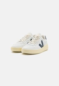 Sneakers bianchi in pelle con accenti blu navy, superficie testurizzata, punta rotonda e suola in gomma beige. Presentano perforazioni e lacci piatti.