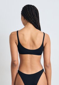 Top bikini nero con spalline sottili e scollatura rotonda, abbinato a un fondo a vita bassa coordinato, entrambi realizzati in tessuto morbido.