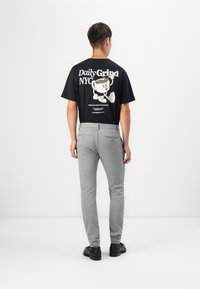 Camiseta gráfica negra con un personaje de dibujos animados y texto, combinada con pantalones ajustados de color gris claro, hechos de material suave. Zapatos negros.