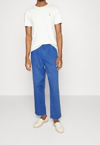 Vit t-shirt med kort ärm och en liten emblem, ihop med blå vida byxor och ljusbeige espadrillos.