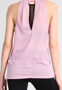 Tank top deportivo de color rosa claro que presenta una tela de malla, cuello halter y un corte en la parte posterior con un panel negro en contraste.