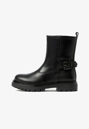 Stivale alla caviglia in pelle nera con punta arrotondata, pannello elastico laterale e dettaglio con fibbia sulla cinghia alla caviglia. Suola in gomma scanalata per una maggiore trazione.
