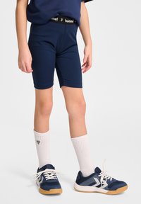 Mörkblå shorts med svart midja som har "hummel"-logotyp, i kombination med vita knästrumpor och marinblå sportskor.