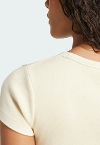 Lühikeste varrukatega ribakujuline särk heledas kollases. Omab ümarat kaelust ja pehmet tekstuuri, millel on nähtavad õmblused õlgadel.