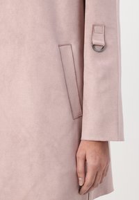 Lyst rosa faux suede-kåpe med rett snitt. Har en sidelomme og en løkke detalj på ermet. Jevn tekstur.