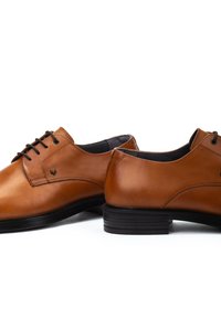 Chaussures habillées en cuir tan avec des orteils ronds, un laçage à six œillets, des semelles en caoutchouc noir, une texture lisse et un discret logo sur le côté.