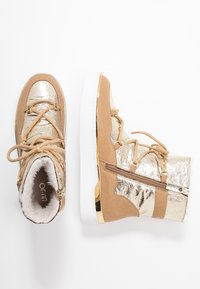 Stivaletti alla caviglia color sabbia e oro con una parte superiore metallica, accenti in suede, design con lacci, cerniera laterale e una spessa suola bianca.
