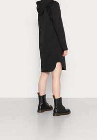 Černá mikinošaty s lemem se bočními rozparky, doplněná černými šněrovacími bojovými botami s texturovanou podrážkou a barevnými poutky.