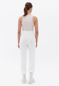 Lichtbeige tanktop gecombineerd met witte gebreide broeken. De broeken hebben een elastische tailleband en worden gedragen met witte enkellaarsjes. Soepele texturen.