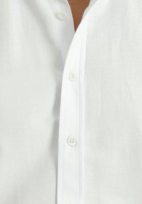 Biała koszula z guzikami, wykonana z teksturowanej tkaniny. Posiada stójkę oraz pięć białych guzików z przodu, co podkreśla klasyczny styl.