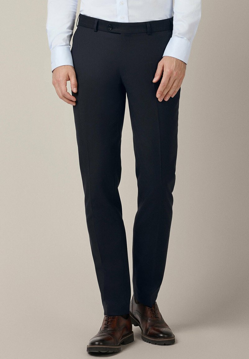 Granatowe spodnie o slim fit, z płaskim przodem, paskami na pasek i pojedynczym zapięciem na guzik. Noszone z brązowymi butami eleganckimi.