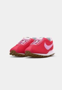 Par de tênis de corrida Nike em malha vermelha com logótipos em swoosh rosa e solas brancas sobre um fundo branco liso.