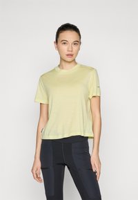 Short-sleeve, light yellow athletic t-shirt with a rounded neckline and a relaxed fit, paired with black leggings featuring side pockets.