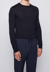 Mörkblå långärmad stickad tröja med rundad hals, med en slät textur och en figurnära design, kombinerad med mönstrade mörkblå byxor.