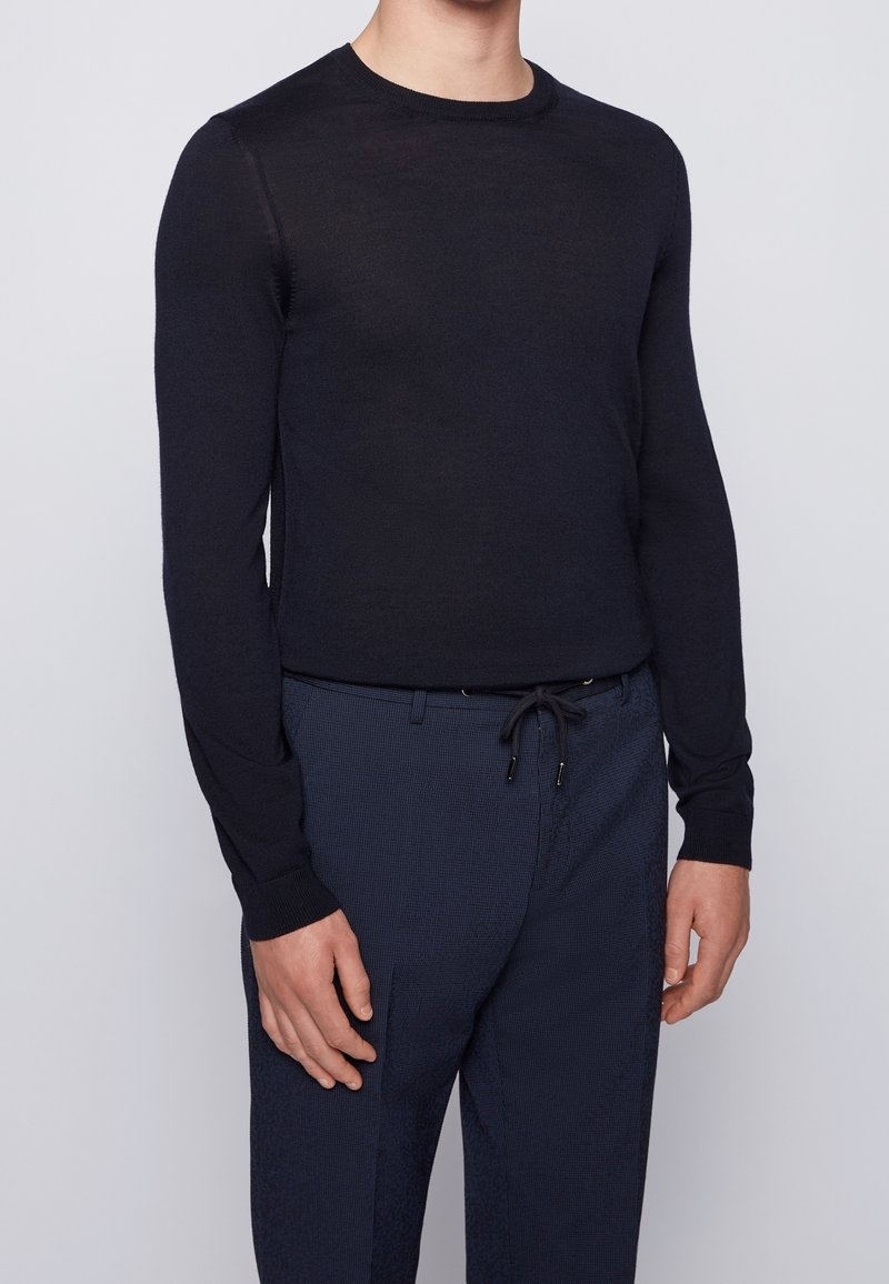 Mörkblå långärmad stickad tröja med rundad hals, med en slät textur och en figurnära design, kombinerad med mönstrade mörkblå byxor.