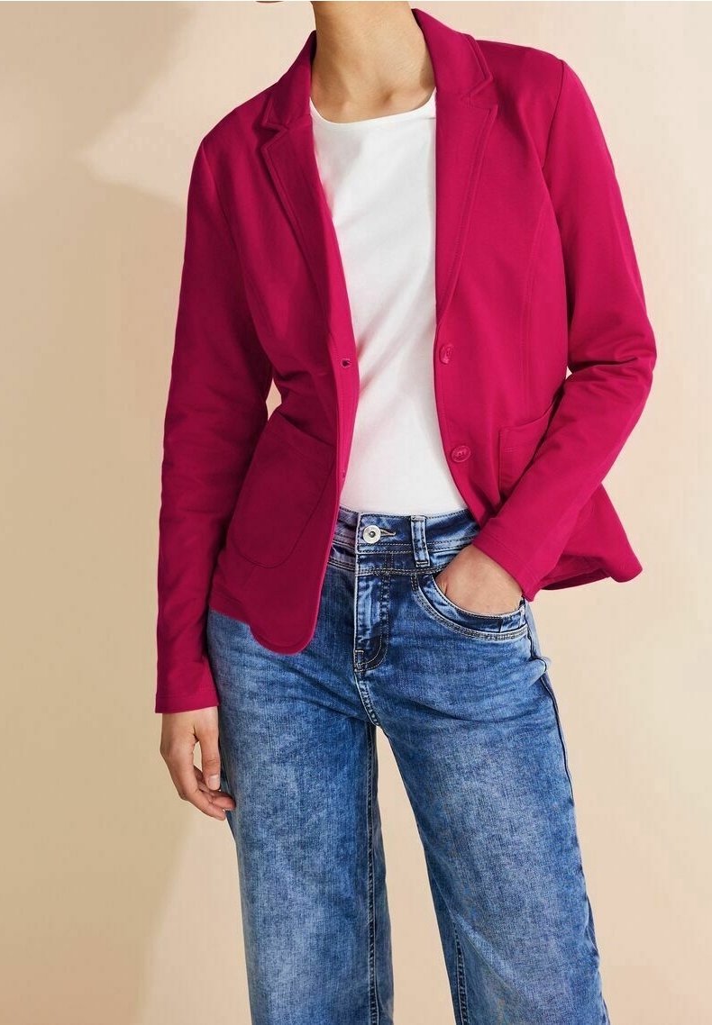 Blazer fuchsia à coupe ajustée, fermeture à bouton unique et deux poches avant, associé à un jean bleu clair à jambes larges.