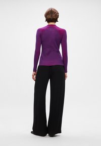 Top de malha roxa ajustado com mangas longas, costuras raglan e decote redondo. Combinado com calças largas pretas.