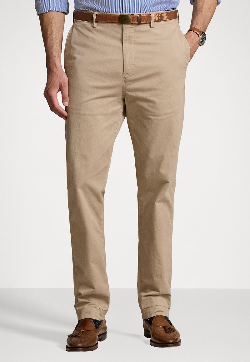 Béžové bavlnené chinos nohavice so rovnými nohavicami, vybavené pútkami na opasok a bočnými vreckami. Skombinované s hnedými koženými topánkami a modrou pruhovanou košeľou.