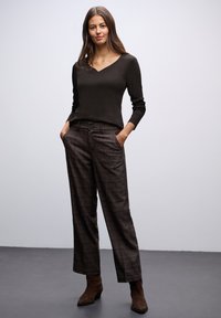Černý top s výstřihem do V a dlouhými rukávy, který je kombinován s volnými hnědými kalhotami s kostkovaným vzorem. Oblečení má texturovanou tkaninu a jemné zdobení se dvěma knoflíky.