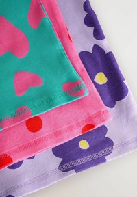 Tre T-shirt impilate: verde con cuori rosa, rosa con pois rossi e lavanda con fiori viola e centri gialli. Tessuto di cotone morbido.