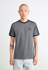 Gray short-sleeve T-shirt with black ribbed collar, three black stripes on shoulders, and small black Adidas logo on left chest.