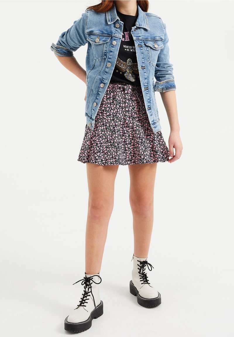 Jeansjacka i ljusblått, svart blommig kjol med rosa accenter och vita snörstövlar med svarta sulor.