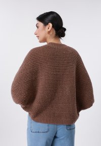 Καφέ πλεκτό πουλόβερ με υφή, στρογγυλή λαιμόκοψη και φαρδιά μανίκια. Συνδυάζεται με ανοιχτόχρωμο τζιν.