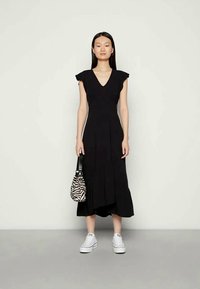 Vestido preto midi com mangas curtas, decote em V, saia plissada, combinado com sapatilhas brancas e uma pequena bolsa às riscas zebra. Textura suave.