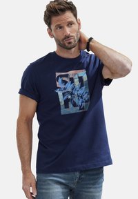 Navyblaues Baumwoll-T-Shirt mit einem grafischen Druck von Blättern in einem strukturierten Design in verschiedenen Blau-, Gelb- und Rosatonen. Kurze Ärmel.