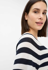 Stripet sweater i marineblå og creme, der har en afslappet pasform med en bred halsudskæring og blød strikket tekstur. Tydeligt synlige striber.