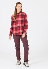 Rød og pink ternet flannel skjorte med knapper, parret med mørke bordeaux bukser med knælapper og grå vandresko med snørebånd.
