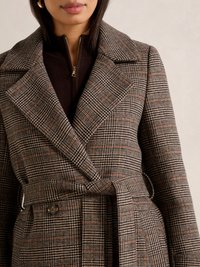 Cappotto a doppio petto in misto lana a quadri marrone e nero con vita cinturata, grandi risvolti e due tasche frontali. La texture è morbida e strutturata.