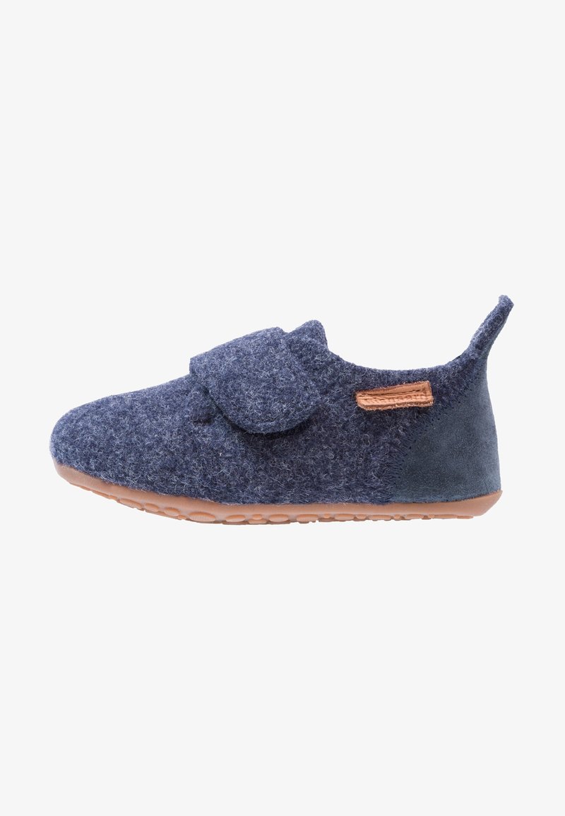 Chaussure bébé bleu marine douce avec une large bride velcro, semelle en caoutchouc marron, talon en daim, et une petite étiquette en cuir cousue sur le côté.