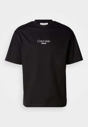 Musta puuvillainen t-paita, jossa on pyöreä kaula-aukko, lyhyet hihat ja valkoinen "Calvin Klein JEANS" -logo edessä. Yksinkertainen ja suora leikkaus.