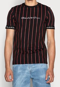 Czarny t-shirt z krótkim rękawem, w czerwone pionowe paski, z białym haftowanym tekstem na piersi i rękawach, o dopasowanym kroju i wykonany z bawełny.