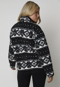 Pullover in pile bianco e nero con motivi geometrici e collo alto. Maniche lunghe, vestibilità rilassata e tessuto testurizzato.
