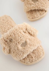 Beige pehmeät tossut, joissa on pehmeä ja pörröinen koostumus, koiran kasvomuotoilu, avonaiset varpaat ja beiget kangaspohjat.