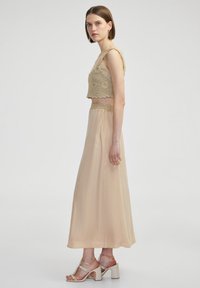 Beige gehaakte crop top met een gekartelde zoom, gecombineerd met een lange, vloeiende beige rok. Bevat subtiele glans en elegante, straps blockhakken sandalen.