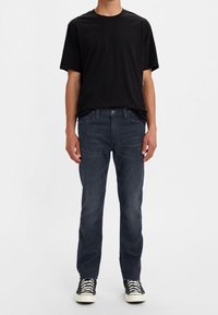 Camiseta negra de algodón combinada con jeans azul oscuro. Los jeans tienen un ajuste clásico con bolsillos y una sutil textura deslavada. Zapatillas negras completan el look.