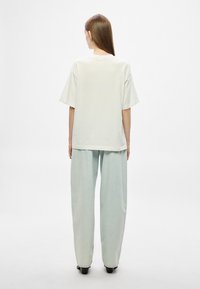 Valge ülisuure lõikega lühikeste varrukatega t-särk, mida kannavad helesinise laiade säärega teksadega. Sile tekstuur ja vaba lõige, vaadatuna tagant.