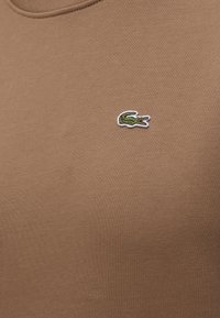 Tissu de polo marron avec un petit logo crocodile vert brodé sur la partie gauche de la poitrine.