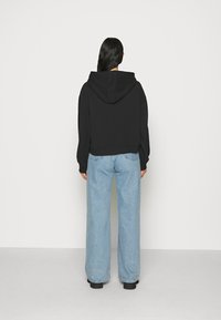 Kort svart huvtröja med en huva, tillsammans med ljusblå vida jeans. Tyget verkar mjukt och jeansen har en urblekt finish.